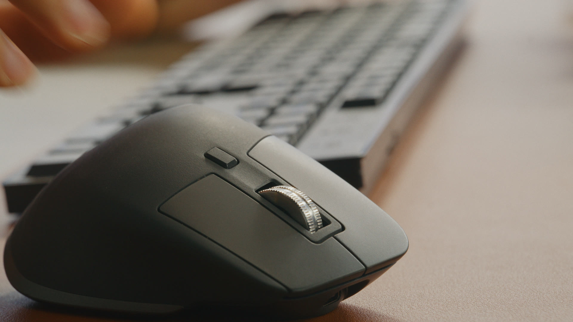 Macro side-on close-up of a calm hand on a silver Logitech mouse with the metal scroll wheel visible.