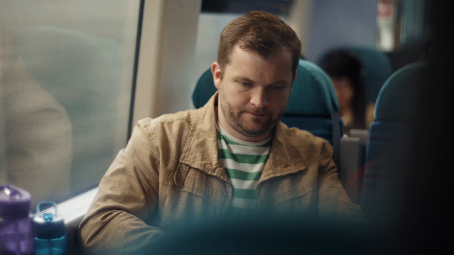 Cinematic MCU of Dad in tan check shirt over a green-and-white striped tee, smiling knowingly at the kids out of frame, soft window light