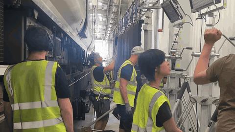 BTS — multiple crew in hi-vis vests assembling the LED panel wall + an Astera-style LED tile lighting tower beside the train carriage, mid-rig
