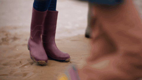 Three pairs of welly boots. green, yellow and rainbow. splashing through shallow tide.