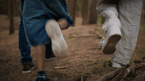 Low-angle of three sets of legs walking through a pine forest path, foreground denim, mid white trousers.