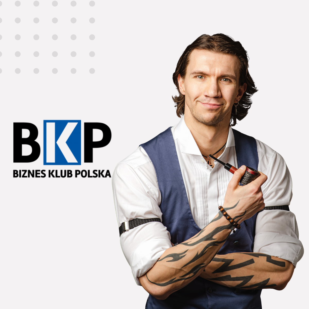 Mężczyzna w eleganckim stroju z tatuażami na przedramionach, uśmiechnięty, trzyma fajkę i patrzy w stronę widza. Obok niego logo Biznes Klub Polska. Wizerunek eksperta wizerunkowo wspierającego artykuł o korzyściach z członkostwa w grupie biznesowej dla pr