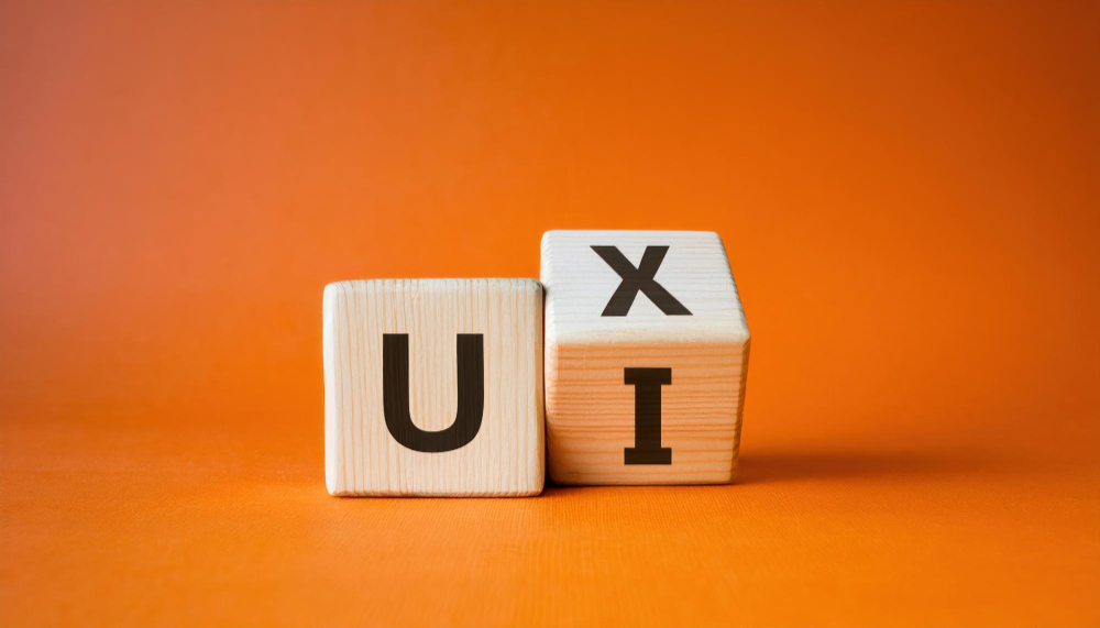 Drewniane klocki z literami U, X oraz I ułożone na pomarańczowym tle, symbolizujące różnice i powiązania między UX a UI designem.