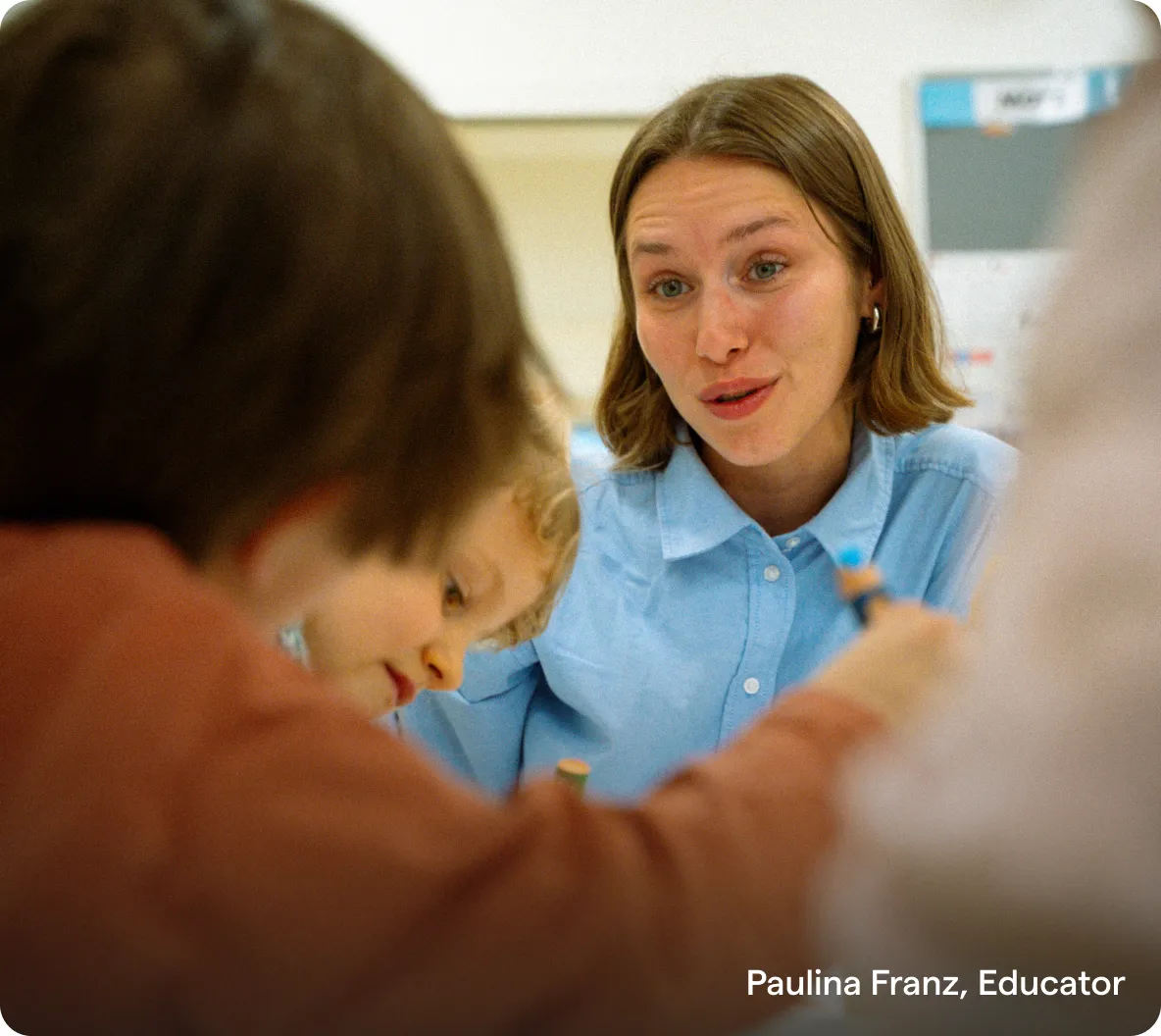 Educator Paulina Franz leaning in attentively while children work on a table activity.