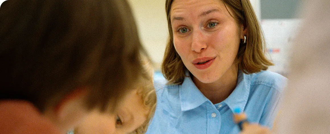 Woman in blue shirt engaging in conversation with two children during an indoor activity.