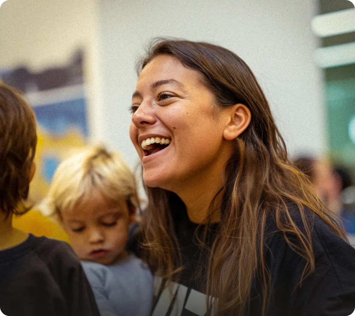 Smiling woman with long hair engaging happily with children in an indoor setting.
