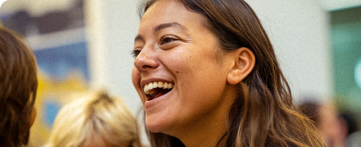Woman smiling and laughing with blurred people and wall art in the background.
