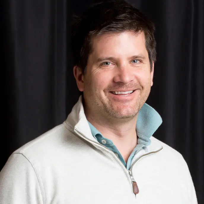 Smiling David Hughes in a studio setting with soft light and dark background
