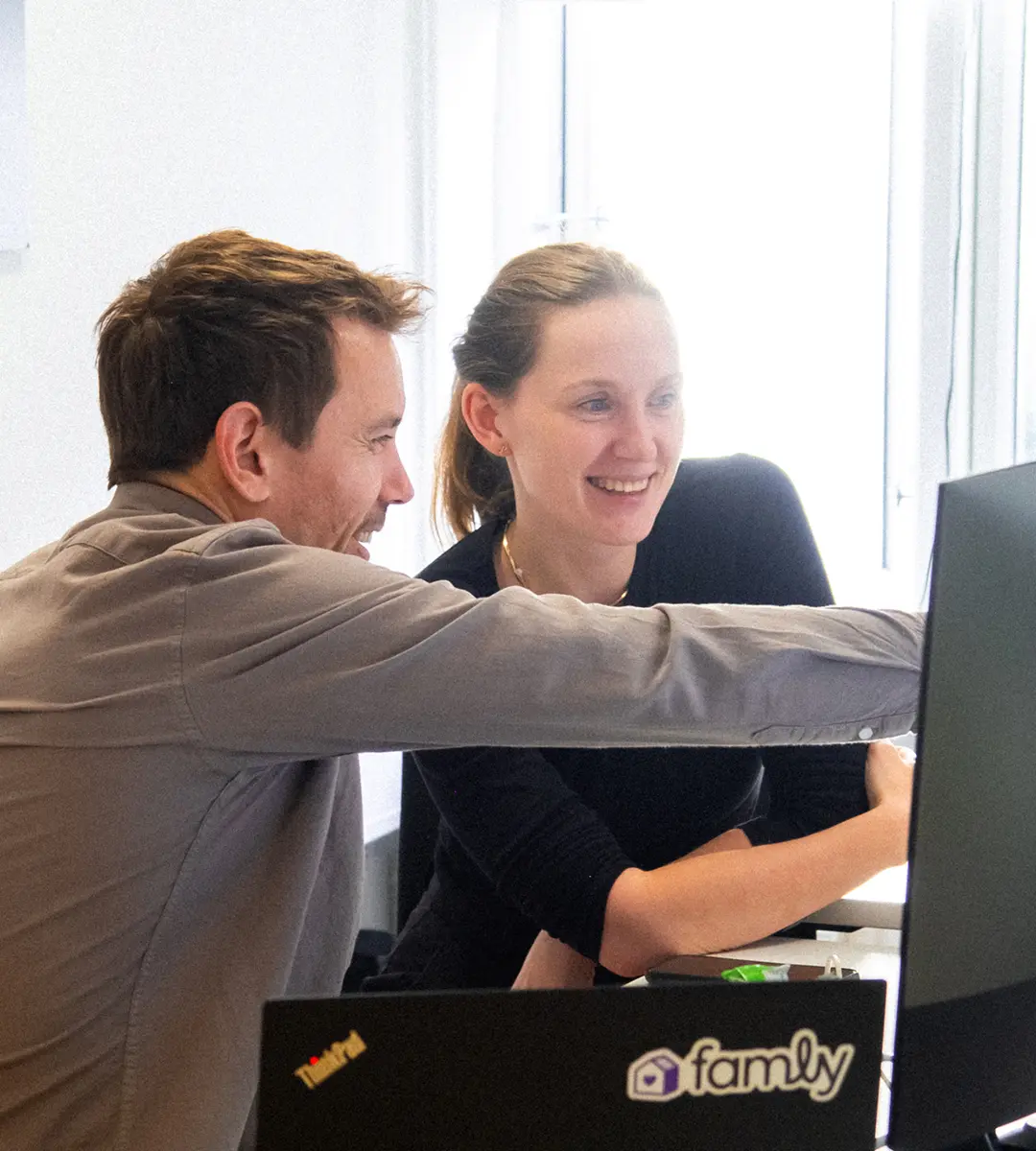 Zwei Kollegen von Famly, die im Büro lächelnd auf einen Computerbildschirm blicken
