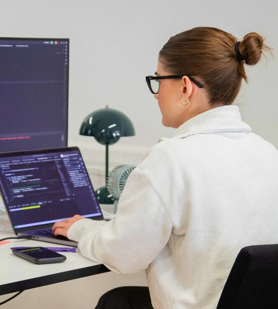 Ein Famly-Entwickler sitzt an einem Schreibtisch und schreibt Code auf einem Laptop und einem externen Monitor