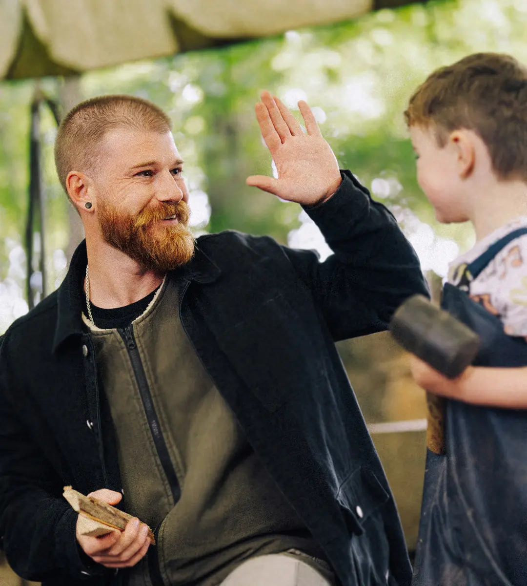 An early years educator high-fiving a young boy outdoors at a nursery