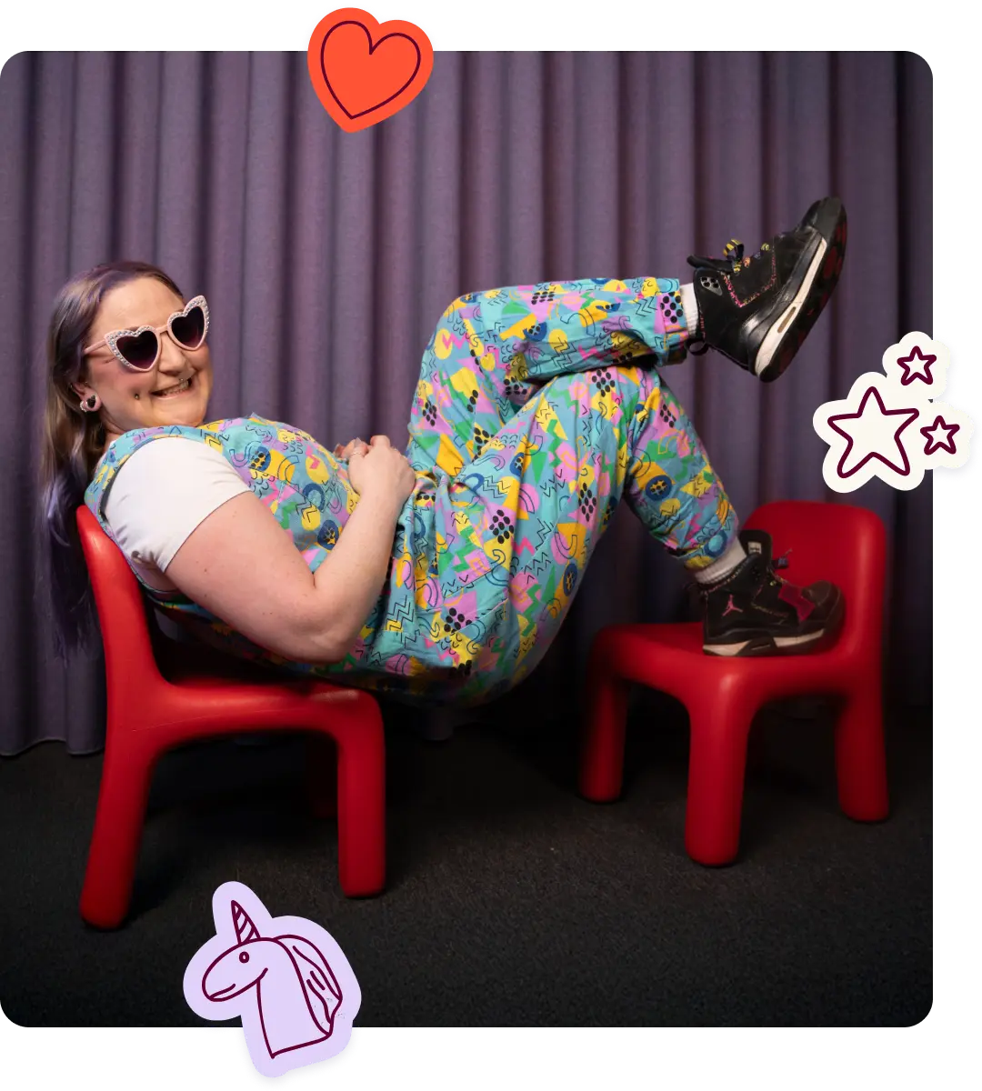 Julia Rose, the podcast host sits in heart-shaped sunglasses lounging across two small red children's chairs