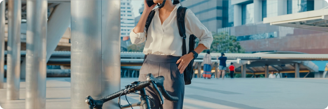 Femme au téléphone, dans une tenue de travail, qui se tient debout derrière son vélo