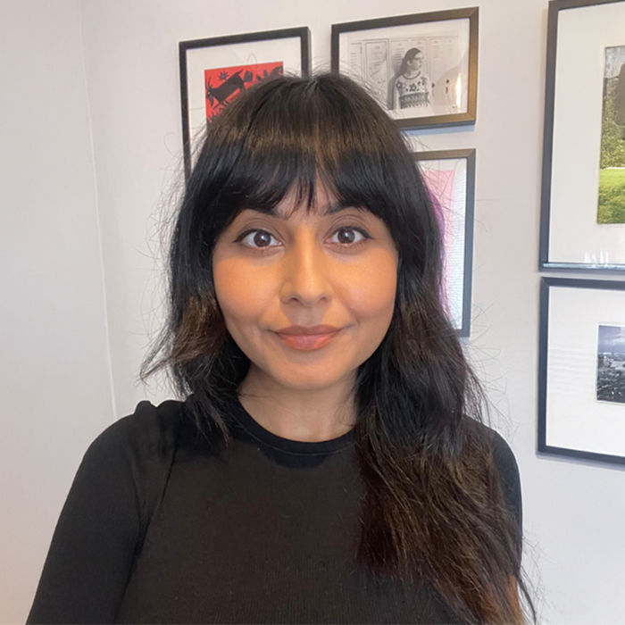 Mr Dot smiling while holding a colourful illustrated book titled ‘Mr. Dot’ in a bright indoor setting, wearing sunglasses, a black shirt, and yellow overalls