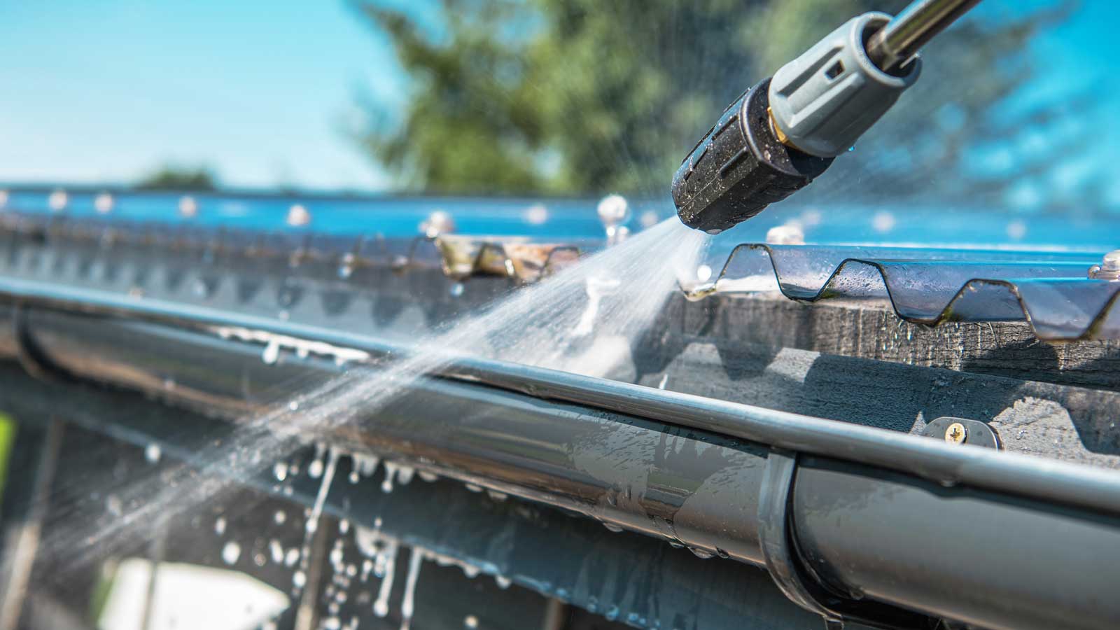 Close up of power-washing wand tip spraying water into a gutter.
