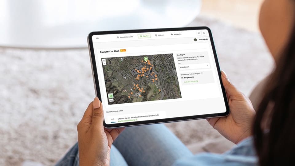Une personne tient une tablette sur laquelle est ouverte l'alerte Houzy Demandes de permis. L'écran affiche une carte satellite avec des marqueurs oranges indiquant les projets de construction actuels dans le voisinage.