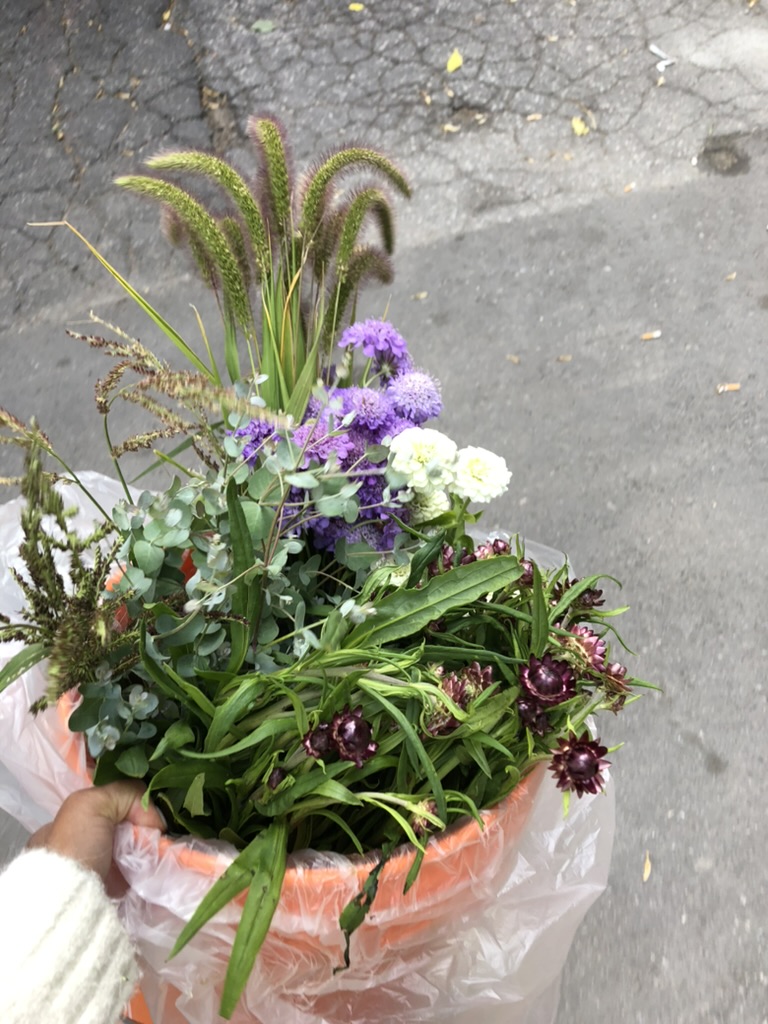 Photograph of Heather Canlas-Rigg holding an orange bucket of flowers during the installation for Eve Tagny’s 2019 Gallery 44 exhibition that she curated. 