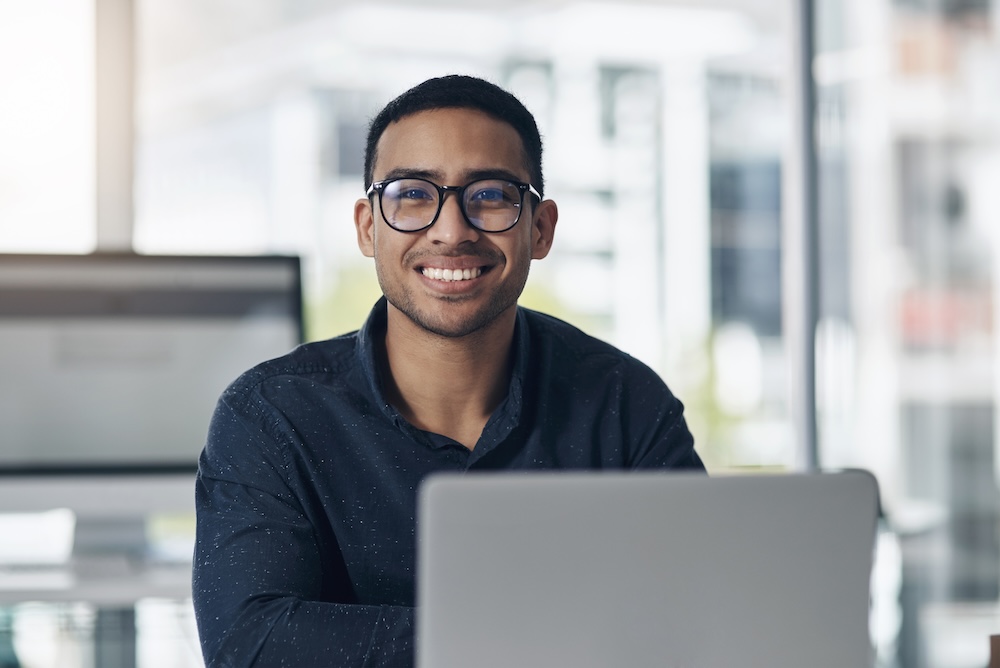 smiling finance officer sitting in his office using his laptop - tithely