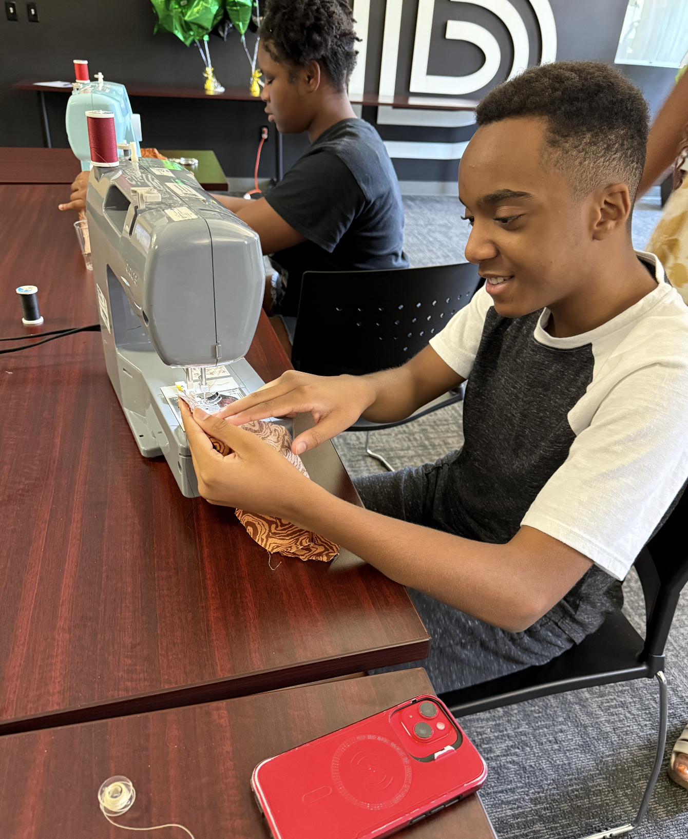A young boy works on a light blue Brother sewing machine, focused on stitching fabric.