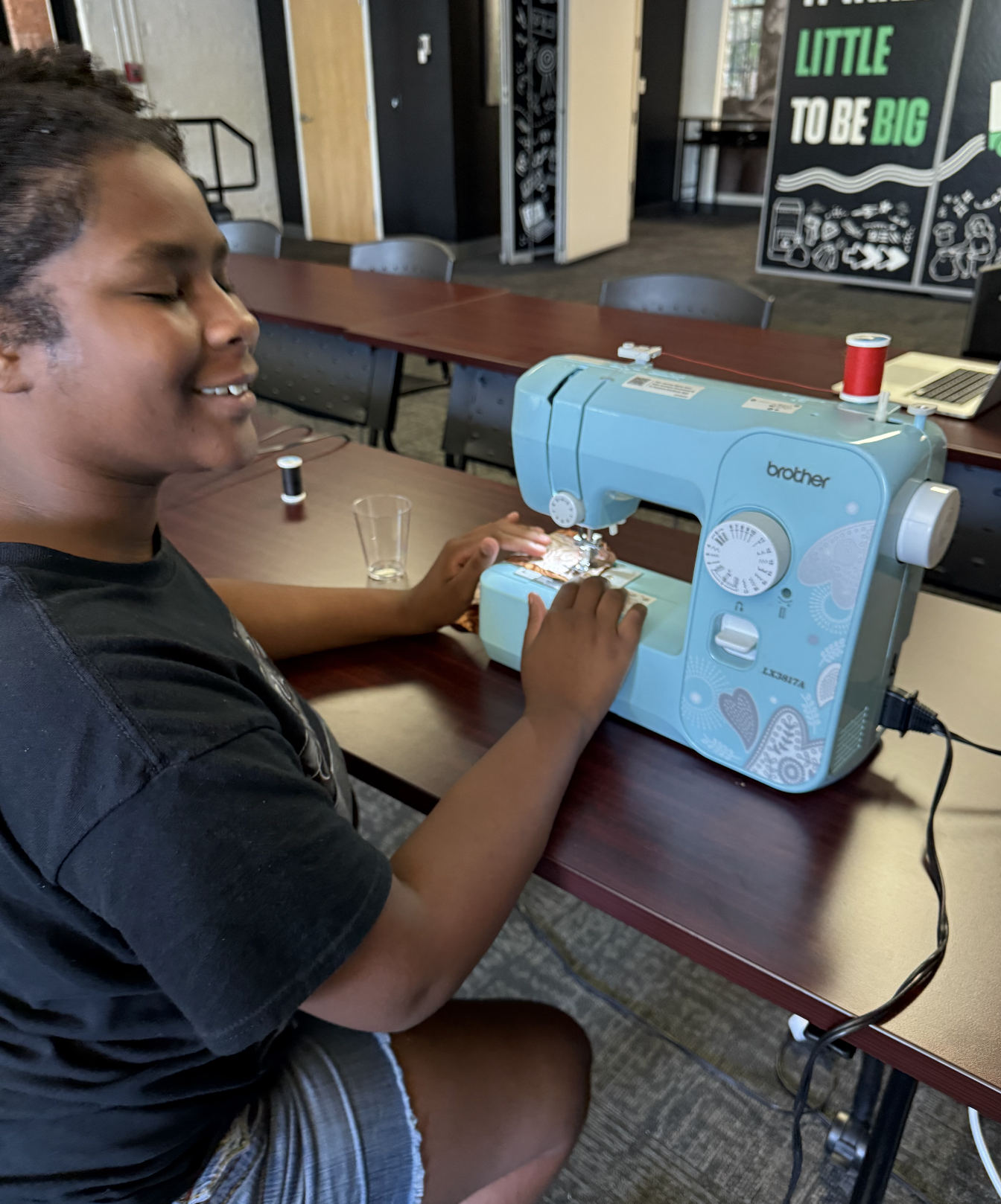 A teenager smiles while operating a sewing machine, stitching patterned fabric.