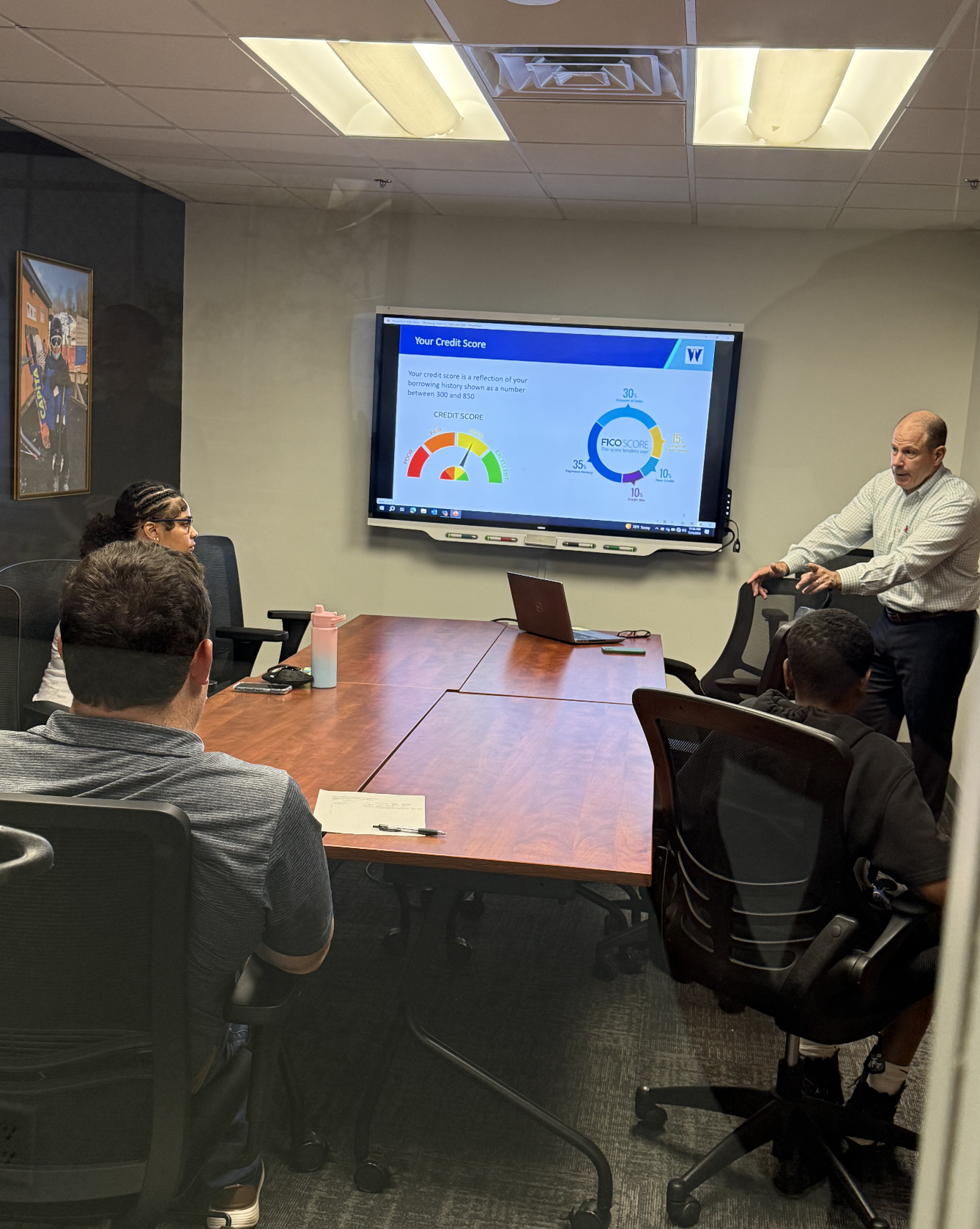 An instructor presents a financial literacy lesson on credit scores to a small group in a conference room with a large screen.