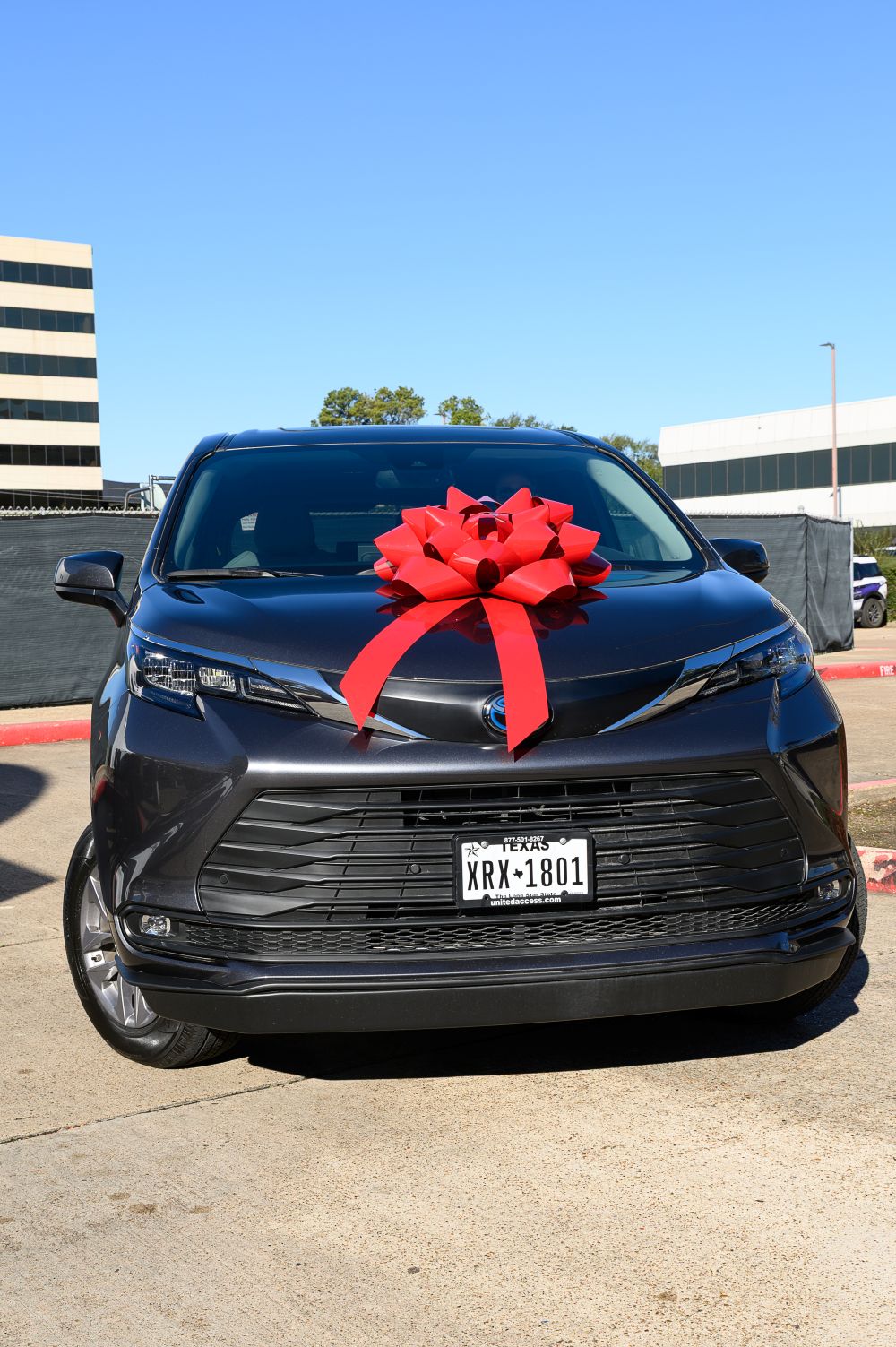Dark gray Toyota Sienna Hybrid wheelchair-accessible van with a large red bow