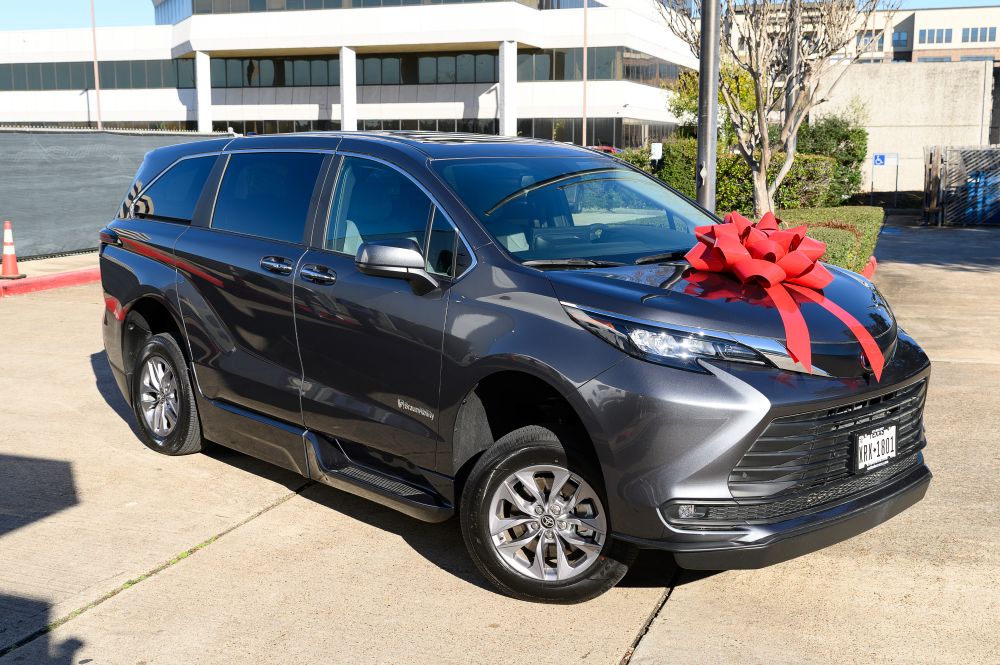 Dark gray Toyota Sienna Hybrid wheelchair-accessible van with a large red bow