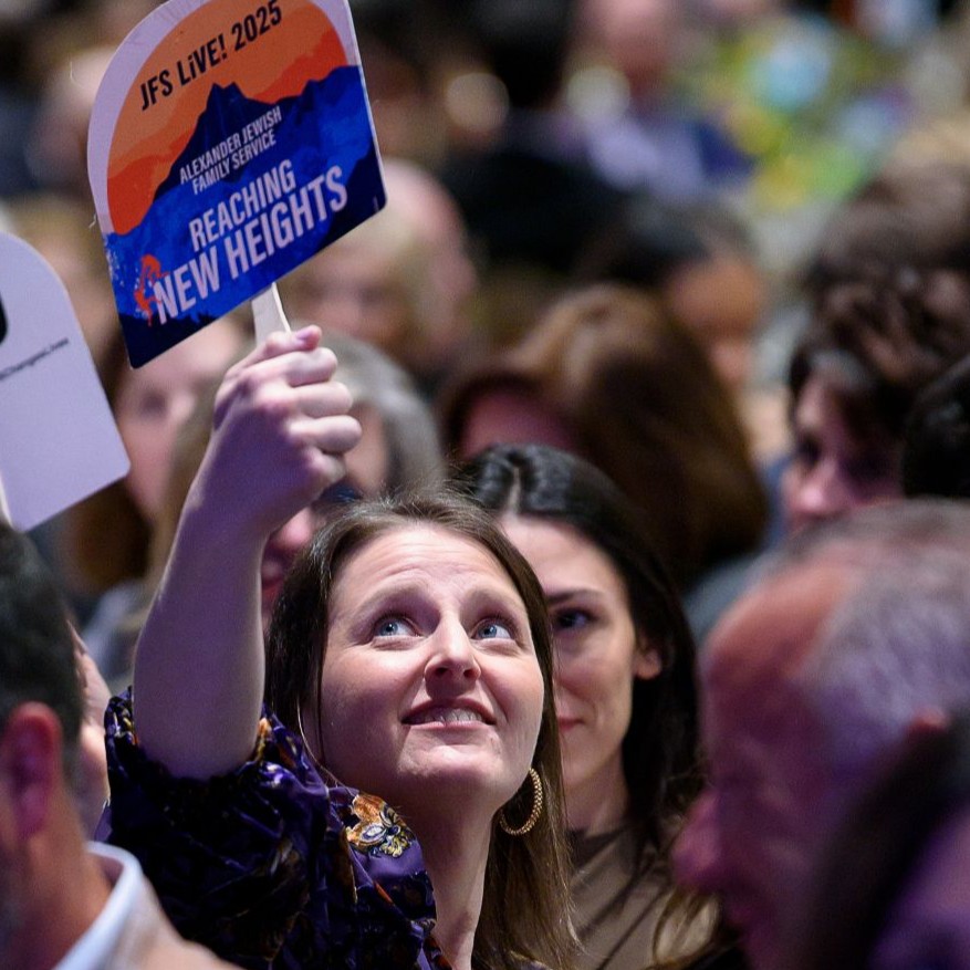 Smiling woman at a gala holds a paddle, surrounded by guests at decorated tables