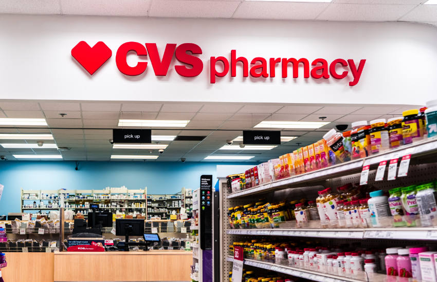 Interior of a CVS Pharmacy store with shelves of health products and a large red CVS Pharmacy sign above the prescription counter.