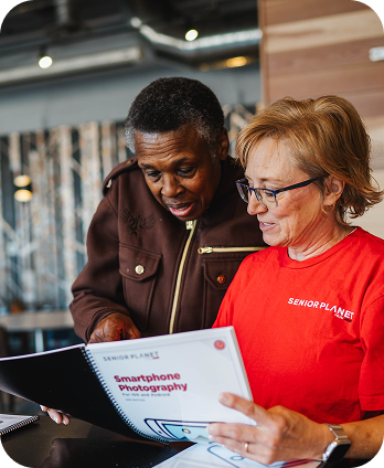 Two older adults review a smartphone photography training workbook together, highlighting digital skills learning and lifelong education.