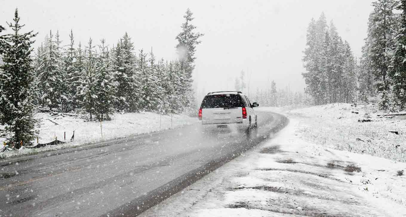 A white SUV on the road road near snow covered trees