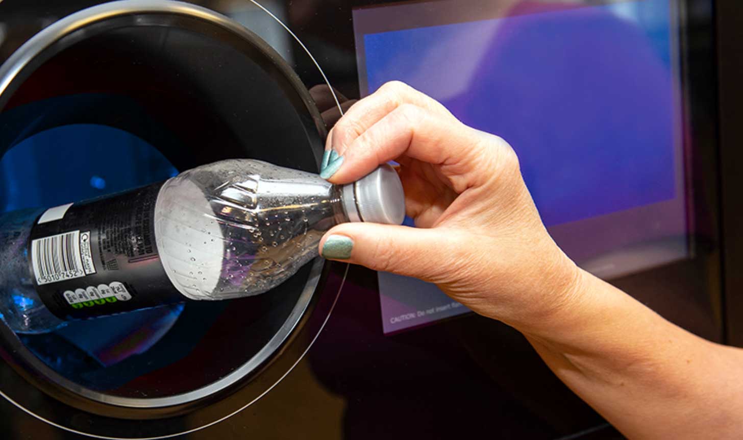 A hand drops a plastic bottle into a circular recycling station