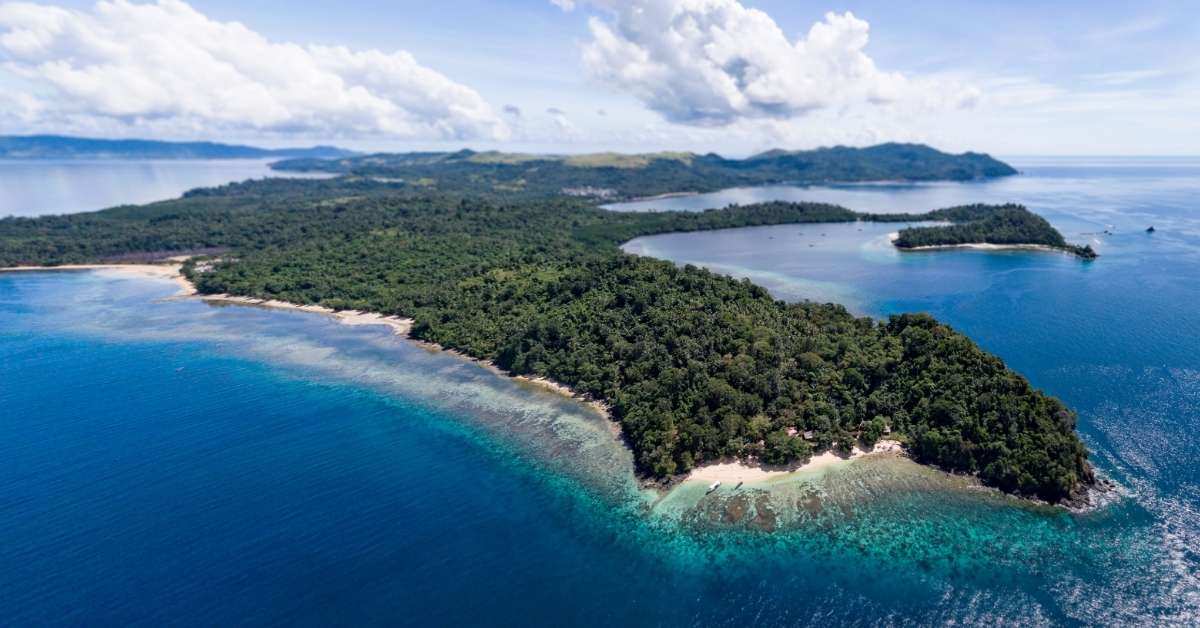 Aerial Panorama of Pulau Bangka in North Sulawesi, Indonesia, an island with trees, lined with sand, and surrounded by gorgeous blue waters.