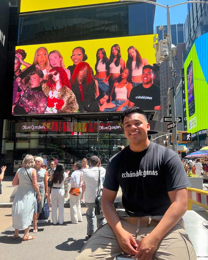 A young man sits under a billboard in Times Square