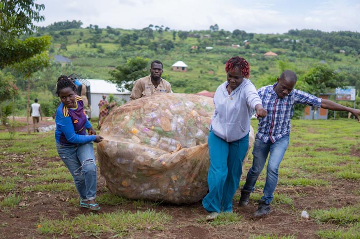 Two women and two men pull an enormous bag full of plastic bottles through the grass in Uganda