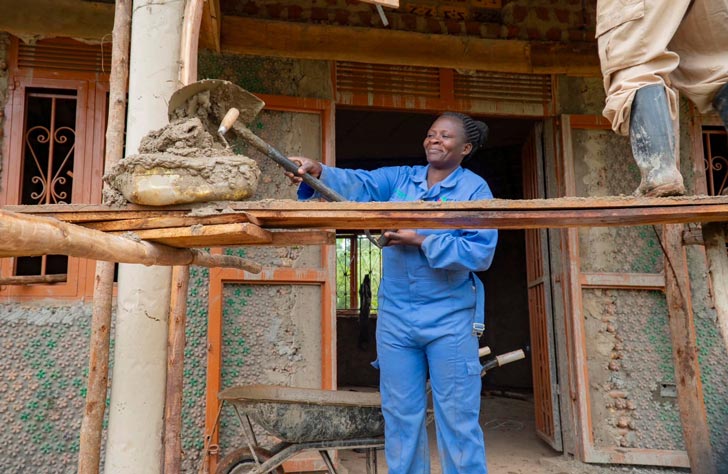 A woman in Uganda shovels cement into a home-building project