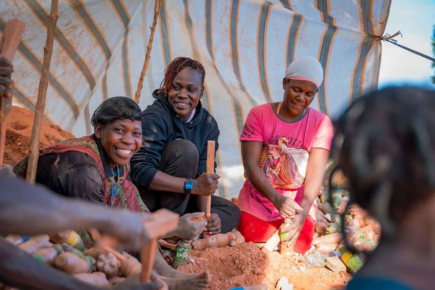Three women dig in the dirt in Uganda as they build a new building