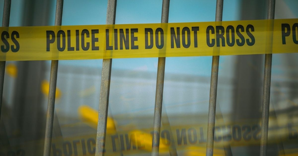 A yellow 'Police Line Do Not Cross' tape plastered on a fence
