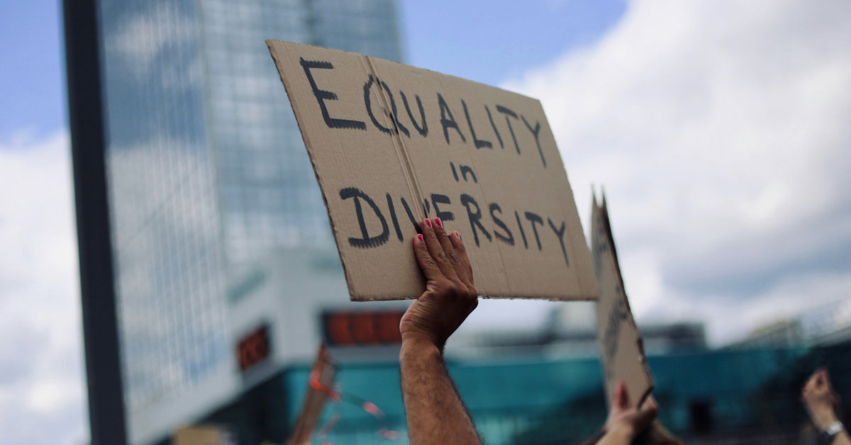 A person holds up a cardboard sign at a protest that reads "equality in diversity"