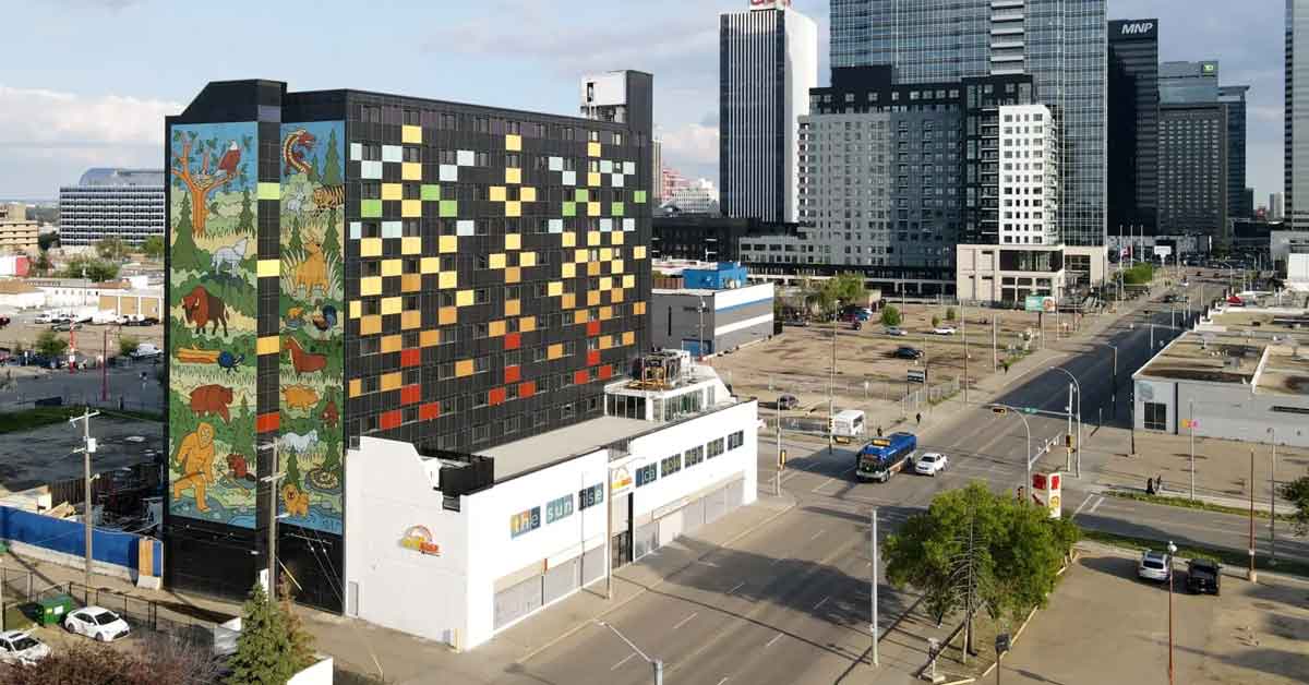 The SunRise Building in Alberta, Canada sits on the corner of a busy street. The exterior of the 12-story residential building is covered in colorful photovoltaic solar panels, forming a mural of animals in nature