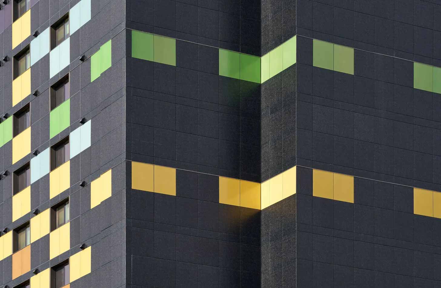 A close-up of colorful solar panels on the exterior of a building, in green, blue, and yellow.