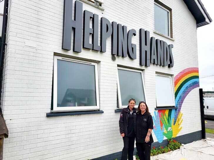 Two women stand in front of the freshly painted Helping Hands building. 