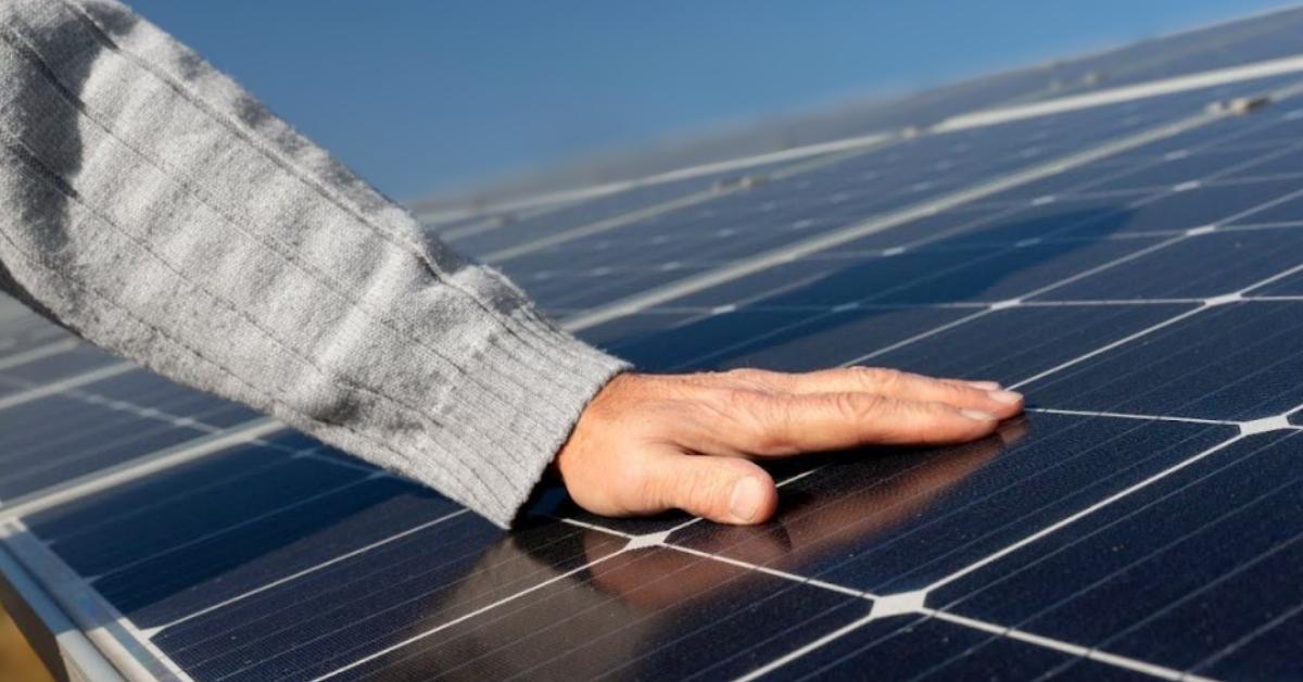 A man places a hand on solar panels in the sun 