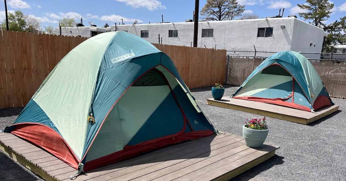 Two green and blue tents sit on wooden palettes in a parking lot