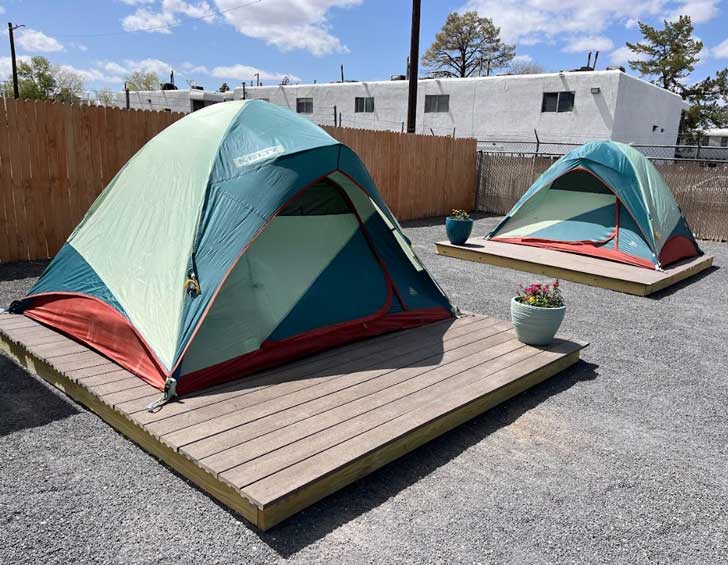 Two green and blue tents sit on wooden palettes in a parking lot