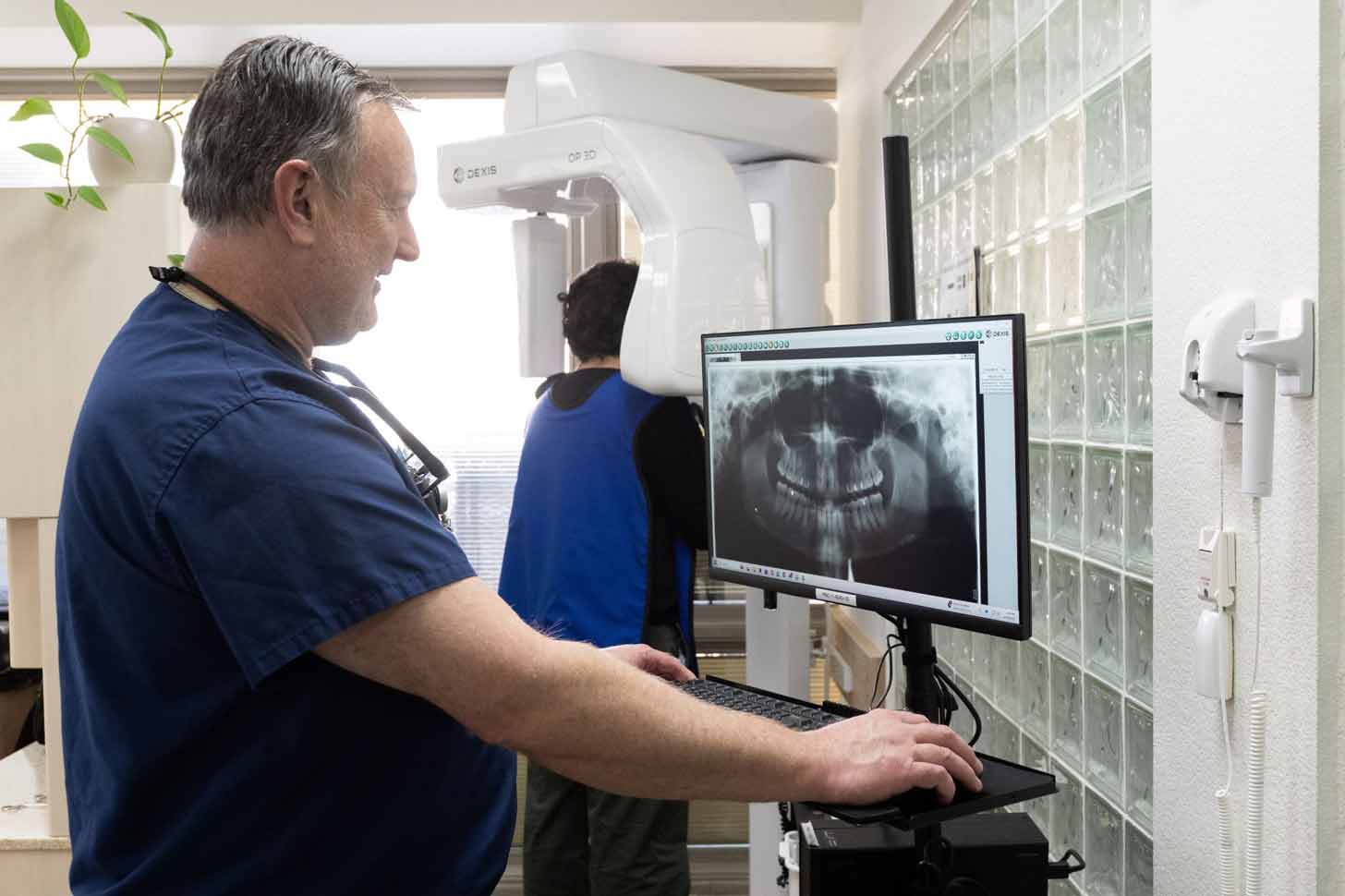 A dentist looks at a computer screen displaying an x-ray image of someone's mouth