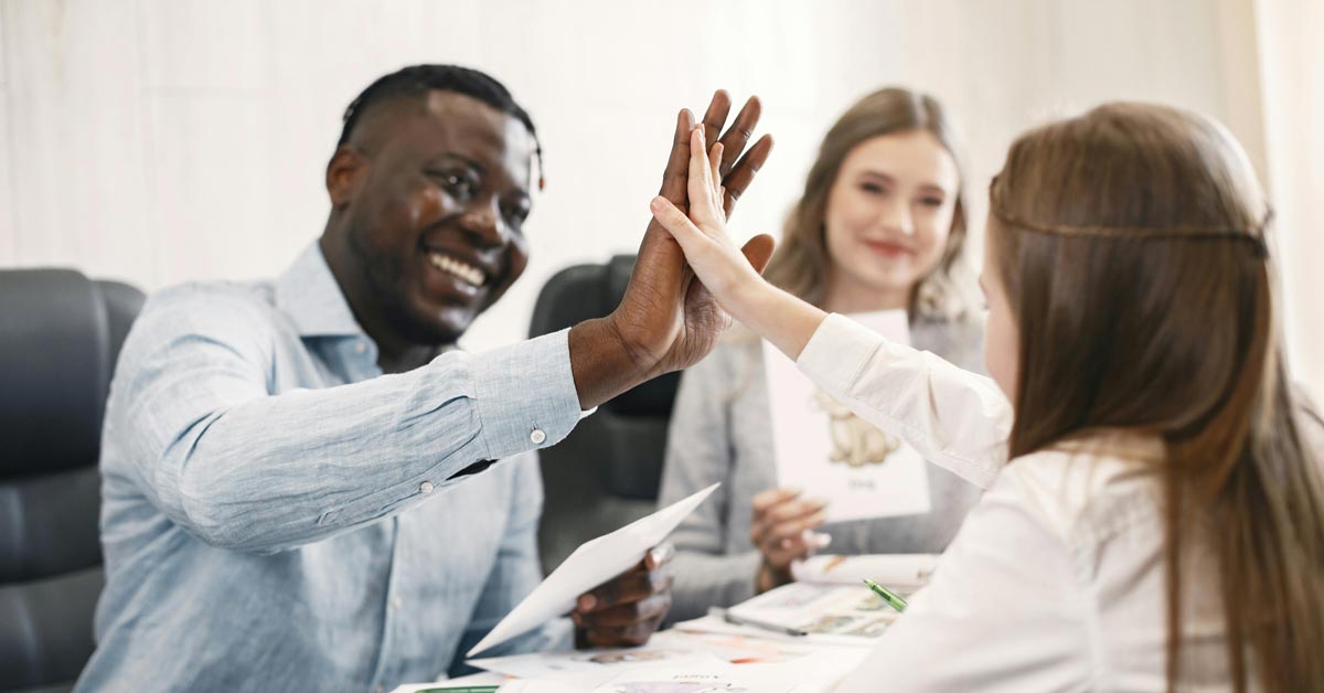A Black male teacher high-fives a white female student