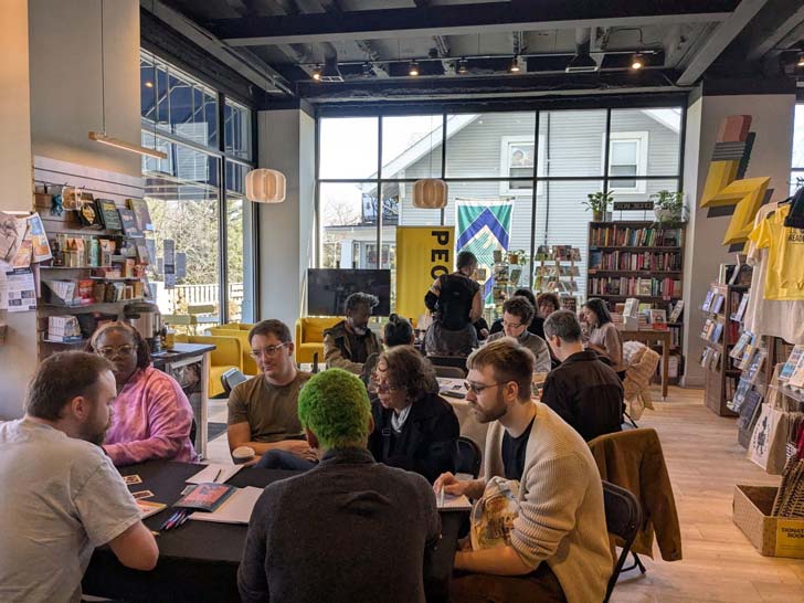A group of people sit at tables inside of People's Book, a small bookstore in Maryland