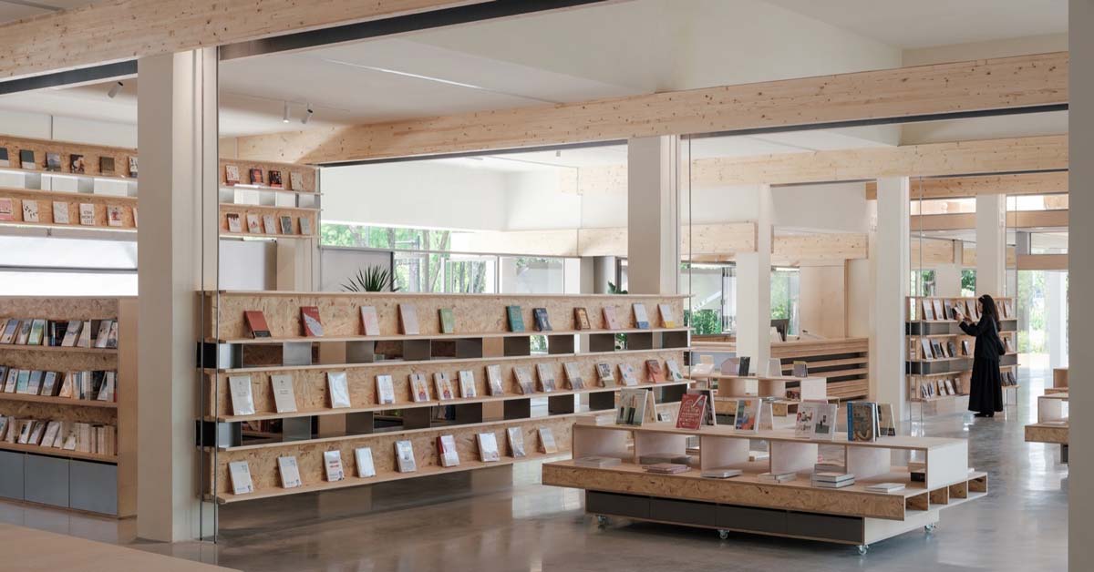 The interior of a well-lit bookstore with light tan timber shelves and luminous columns