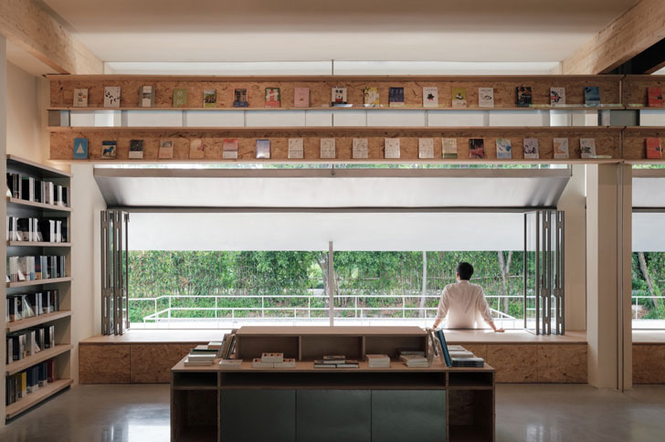 A man in a white shirt sits on a ledge of a bookshop overlooking a green natural area